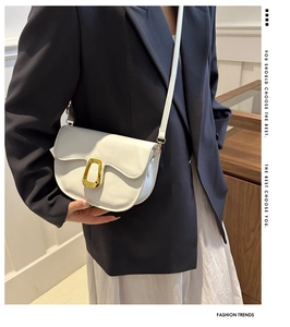 Detail of white saddle bag with golden U-shaped lock on navy blazer and white dress
