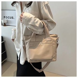 Detail of minimalist beige nylon tote bag featuring front flap pocket and adjustable strap