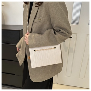 White quilted crossbody bag with gold chain strap worn with a brown blazer suit