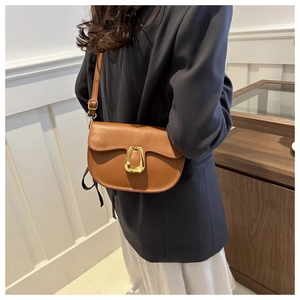 Close-up of caramel leather saddle bag with distinctive matte gold metal clasp and strap