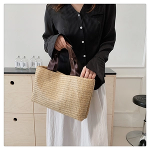 Close-up of woven straw tote bag featuring detailed texture and brown fabric handles