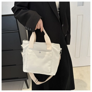Detailed view of beige canvas tote bag with front pocket shown on a model in a black blazer