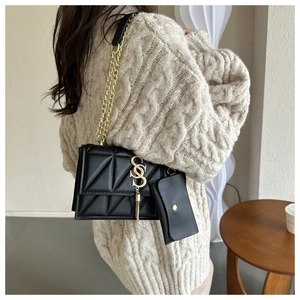 Detail of black quilted crossbody bag with gold chain strap and decorative fringe