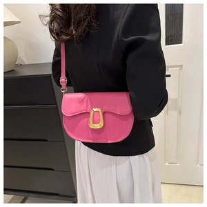 Close-up of a magenta saddle bag with a large gold metal buckle on a woman's shoulder