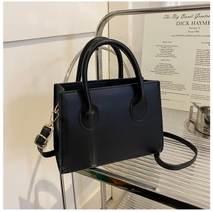 Detail of minimalist black crossbody bag with gold hardware on a metallic shelf