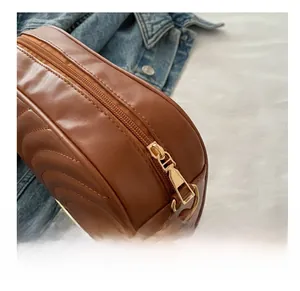 Detail of smooth gold metal zipper on brown quilted crossbody bag with woven strap