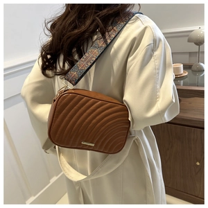 Close-up of brown quilted camera bag with bohemian jacquard strap on beige coat