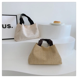 Close-up of woven straw tote bags in beige and brown colors with black fabric handles