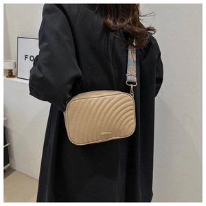 Detail of tan quilted crossbody bag featuring a colorful bohemian woven wide strap