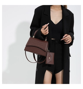 Detalle de bolso marrón oscuro con patrón de cocodrilo, asa trenzada y mini monedero