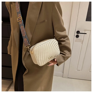 Detail of off-white quilted crossbody bag featuring elegant wave pattern and geometric strap