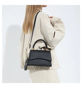 Detalle de bolso negro con textura de cocodrilo, asa trenzada y correa ajustable