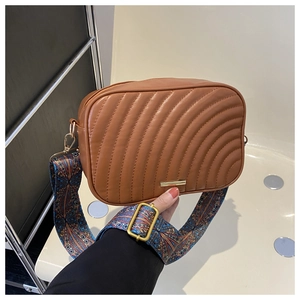Détail du sac caméra matelassé caramel avec large bandoulière imprimée et finitions dorées