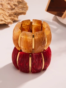 Detail of wide stretch resin bracelets with marble amber and crimson textures in gold