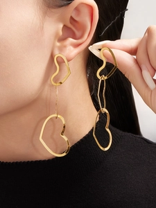 Detail of long hollow heart drop earrings in gold finish worn by a model