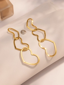 Close-up of golden triple-heart cutout earrings on white leather texture background