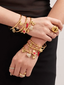Détail de bracelets plaqués or 18k avec breloques et bagues empilées sur un poignet femme