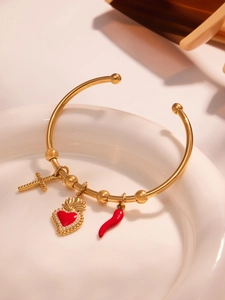 Détail d'un bracelet doré 18 carats avec breloques cœur rouge et croix sur une assiette
