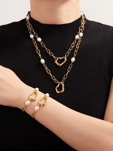 Detailed view of layered gold heart necklaces and pearl bracelets worn on black knitwear