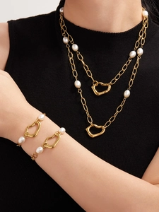 Detail of layered gold necklaces and bracelet with pearls and irregular heart charms