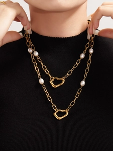 Macro detail of gold layered necklace with white pearls and irregular heart pendants