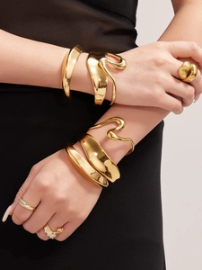 Detalle de brazalete dorado ondulado y anillo de cúpula texturizado en modelo con negro