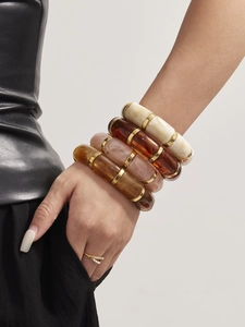 Macro shot of layered resin cylinder bracelets in amber and ivory with gold metal rings
