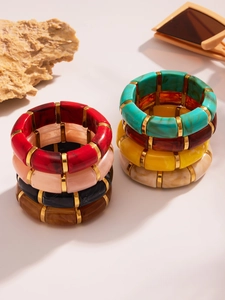 Colorful resin bangles featuring marble patterns and gold metal spacers on warm stone