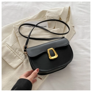 Detail of minimalist black saddle bag with irregular gold buckle on a beige suit