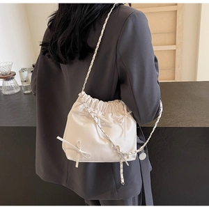 Chic white drawstring bucket bag with bow accents and silver chain strap shown on model