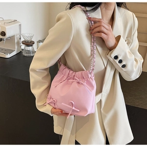 Pink drawstring bucket bag with bow details and chain strap shown on model in a cafe