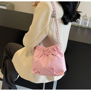 Pink drawstring bucket bag with decorative bows and silver chain strap worn by a model