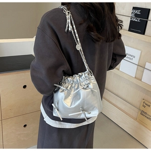 Macro detail of a silver drawstring bucket bag with decorative bows and chain strap