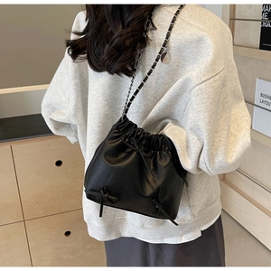 Close-up of black drawstring bucket bag featuring delicate ribbon bows and silver chain strap