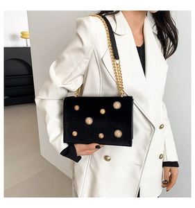 Detail of black velvet crossbody bag with gold sunburst rivets and elegant chain strap