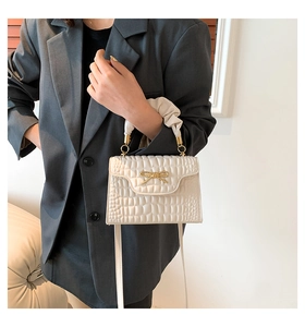 Detail of off-white crocodile embossed crossbody bag with golden bow and pleated handle
