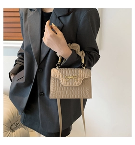 Détail du sac à main beige motif crocodile avec nœud doré et poignée plissée