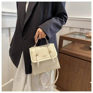 Detail of a cream-white square shoulder bag featuring gold hardware and flap closure