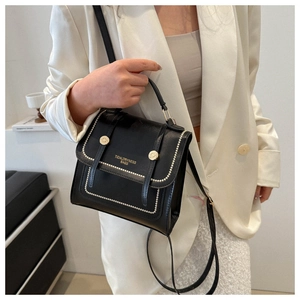 Detail of black leather handbag with gold studs and brand text on white blazer