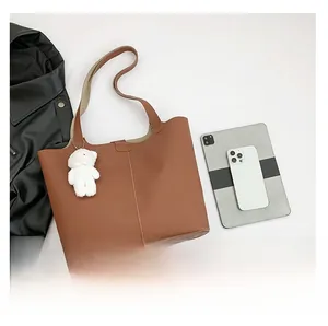 Flat lay of brown litchi grain tote bag with plush bear charm and casual accessories