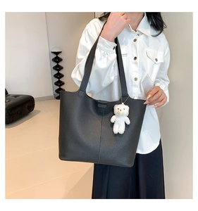 Detail of black pebbled leather tote bag featuring a cute white plush bear charm
