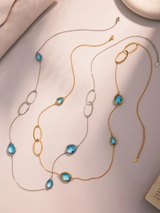 Dettaglio di collane in oro e argento con cristalli a goccia blu su libro e borsa in pelle
