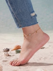Nahaufnahme eines goldenen Fußkettchens mit Diamantanhänger am Knöchel vor Strandkulisse