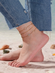 Detailansicht der dreilagigen goldenen Boho-Fußkette mit Zirkonia-Blumen am Strand