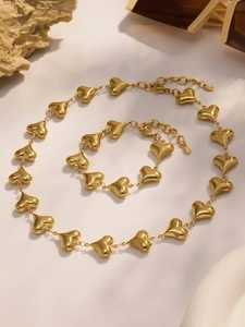 Detail shot of 18k gold plated hollow heart necklace and bracelet set on marble surface
