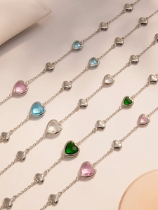 Macro detail of multicolor heart-shaped glass stones and steel links on gold necklaces