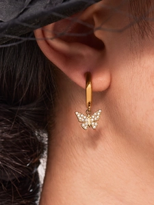 Gros plan d'une boucle d'oreille papillon sertie de cristaux sur un mannequin au chapeau