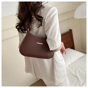 Brown minimalist underarm bag with gold metal clasp shown on model in white shirt