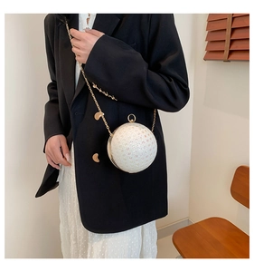 Close-up of white spherical evening bag with pearl texture and gold chain worn by model