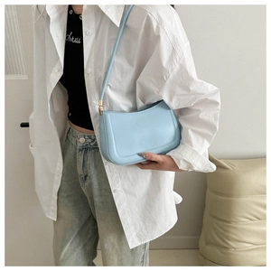 Light blue faux leather underarm bag with curved design shown in a casual lifestyle setting
